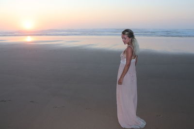 Woman standing on beach against sky during sunset