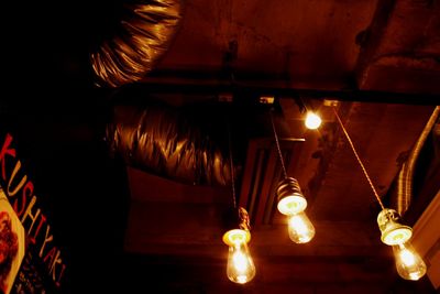 Low angle view of illuminated light bulb hanging at night