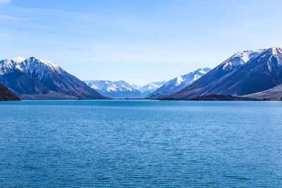 Scenic view of sea and snowcapped mountains against blue sky