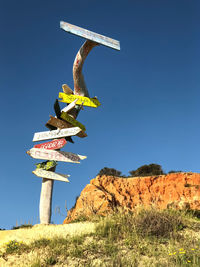 Low angle view of information sign on hill against clear blue sky