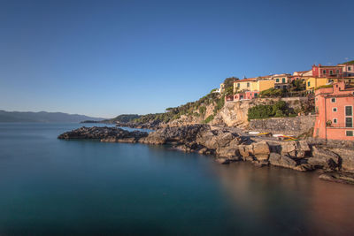 Scenic view of sea by buildings against clear blue sky