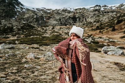 Woman wearing knit hat standing on footpath against field