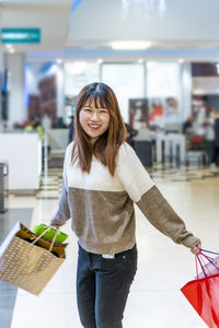 Pretty happy young chinese woman with colorful shopping bags walking into a store