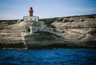 Lighthouse on cliff by sea against clear blue sky