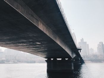 Low angle view of bridge over river in city against sky