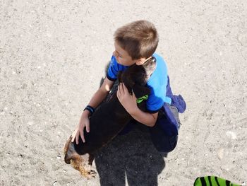 High angle view of boy embracing dog while crouching on sand at beach during summer