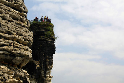 Low angle view of people on rock against sky