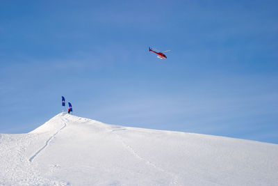 Helicopter flying over snow covered mountain with flags against sky