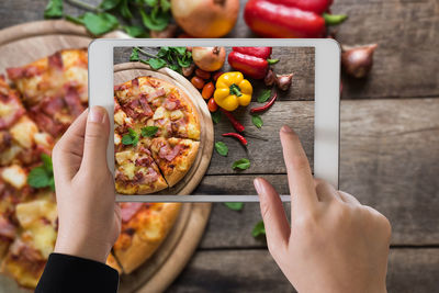Cropped hand of woman photographing food from digital tablet on table