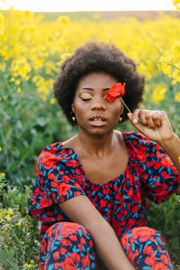 Close-up of young woman holding flower at field