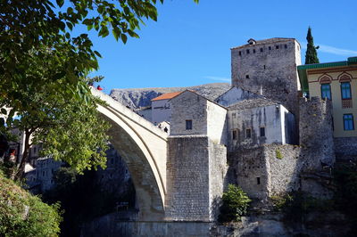 Arch bridge amidst trees and buildings against clear sky