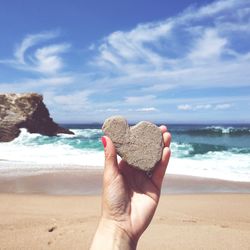 Cropped hand of woman holding heart shape rock at beach during summer
