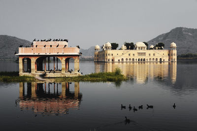 Birds and built structures in lake against clear sky