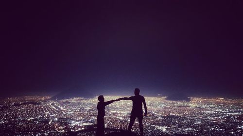 Silhouette men standing on illuminated city against sky at night