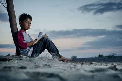 Full length of man sitting on land against sky