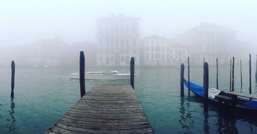 Pier on river against buildings in foggy weather