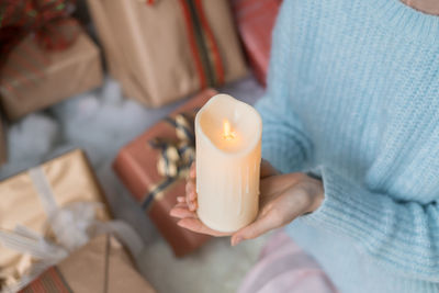 Woman in light blue sweater holding thick white wax candle in her hands. christmas holiday. female
