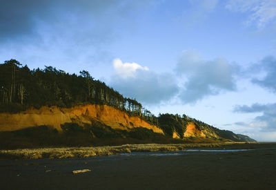 Scenic view of sea by mountain against sky