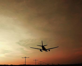 Low angle view of airplane flying against sky during sunset