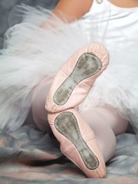 Low section of girl wearing ballet shoes while sitting on bed