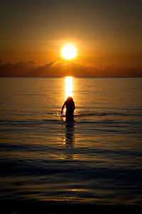 Silhouette man in sea against sky during sunset