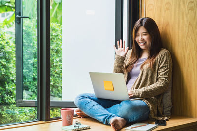 Young woman using phone while sitting on laptop