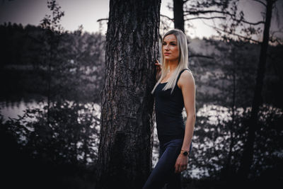 Mid adult woman looking away while standing by tree trunk in forest