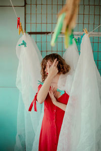 Thoughtful woman in red dress with curtain at home