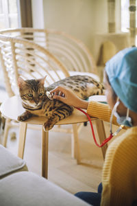 Female veterinarian checking cat's heartbeat with stethoscope at home