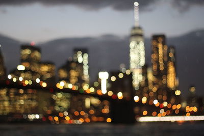 Defocused image of illuminated brooklyn bridge over east river by city against sky at dusk