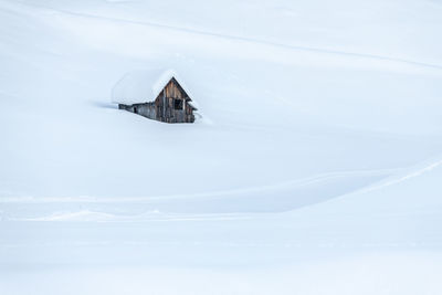 Snow covered house by building against sky