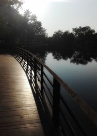 Wooden railing by lake against sky