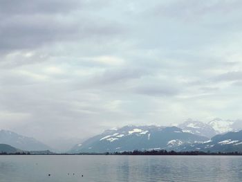 Scenic view of lake by snowcapped mountains against sky