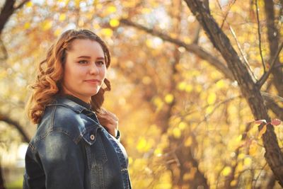 Portrait of young woman with autumn leaves against trees