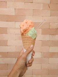 Hand holding ice cream cone against brick wall