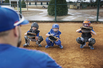 Rear view of coach training baseball catchers on field