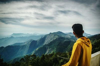 Rear view of man standing on mountain against sky