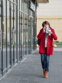 Woman in red coat talks by smartphone. woman walks down street grasping coffee and paper cheque.