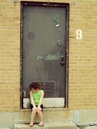 Full length of girl sitting against closed door