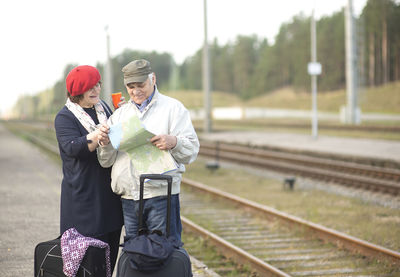 Happy seniors couple with suitcases looking at the map and waiting for the train to go on a trip