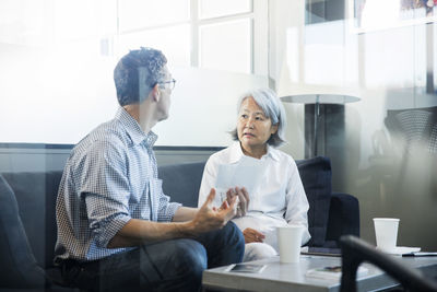 Colleagues discussing while sitting on sofa in office