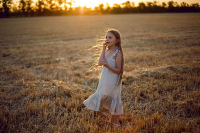 Girl child with long hair walking across the field wearing with long hair during sunset