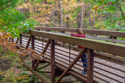 Woman sitting on bench by footbridge