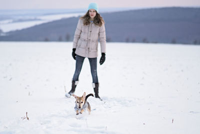Girl walks the small dog in woolen clothes in the snow during winter time