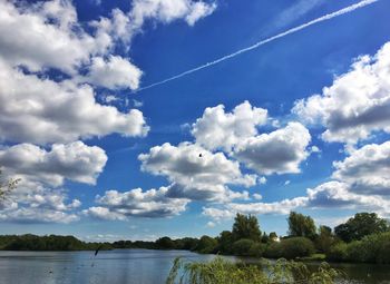 Scenic view of vapor trails over lake against blue sky