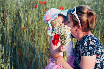 Girl holding flower by mother on grass