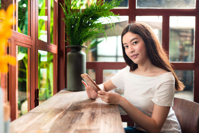 Portrait of young woman using phone while sitting on table