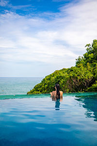 Rear view of woman in infinity pool against sky