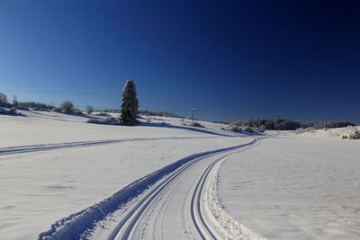 Snow covered landscape against clear blue sky