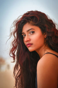 Portrait of beautiful young woman with wavy hair against sky